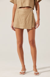 A person is wearing a beige cropped short-sleeve top and a matching beige wrap-style skirt with a single button closure, paired with white open-toe sandals.